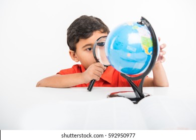 Indian Kid Observing Or Studying Educational Globe Model With Magnifying Glass