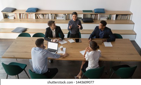 Indian leader manager talk to multiethnic employees team at diverse group meeting, female hindu worker presenting report work result business plan at corporate briefing at conference table, top view