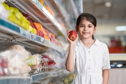 Indian Little Girl Showing Red Apple At Fruit Store.