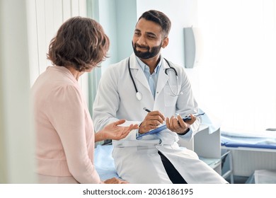 Indian male doctor consulting senior old patient filling form at consultation. Professional physician wearing white coat talking to mature woman signing medical paper at appointment visit in clinic. - Shutterstock ID 2036186195