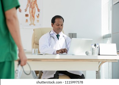 Indian Male Doctor Sitting At His Workplace And Typing On Laptop