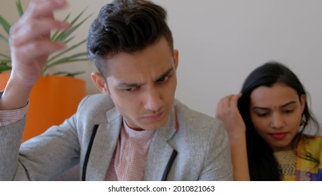 An Indian Male And Female Couple Sitting On A Couch With Looking At Something With Serious Faces