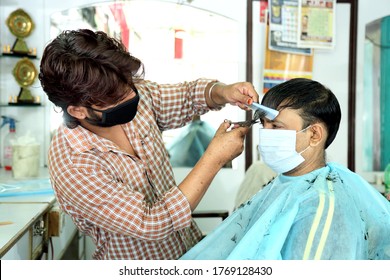 An Indian Male Hair Dresser Cutting Hair In His Beauty Saloon With Proper Safety Measures For Covid-19.Cutting Hair Of A Man In Mask. Hair Care During Covid-19.Beauty Saloon Opens After Lock Down.