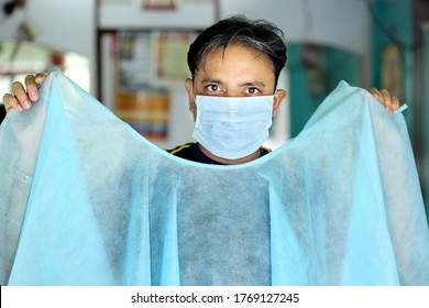 An Indian Male Hair Dresser In Mask Showing Disposable Apron For Hair And Beauty Care With Proper Safety Measures For Covid-19. Safety Measures In Salons. Beauty Saloon Opens After Lock Down.