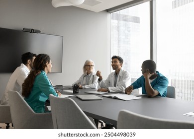 Indian male therapist wear white coat makes speech at group meeting medical seminar in modern conference room. Multiethnic clinic staff members listening opinion, decisions and solutions of workmate - Powered by Shutterstock