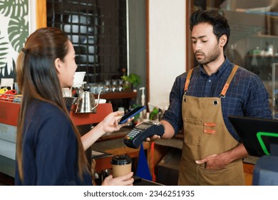 Indian man cafe owner handing over credit card reader Let beautiful female customers scan QR code to pay for coffee and bakery. Reduce contact and no cash payments. insufficient cash In cafe on the go