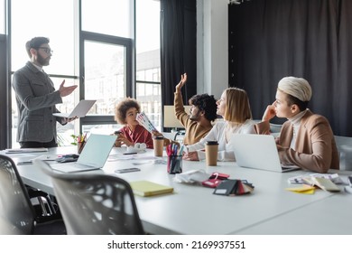 Indian Man With Color Samples Raising Hand During Meeting With Multiethnic Team In Ad Agency