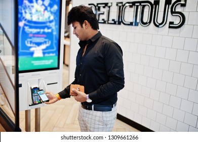 Indian Man Customer At Store Place Orders And Pay By Contactless Credit Card On Mobile Phone Through Self Pay Floor Kiosk For Fast Food, Payment Terminal. Pay Pass.
