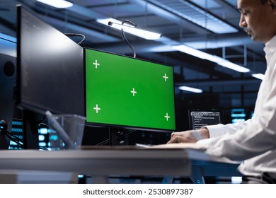Indian man in data center using green screen computer to check for server performance issues. IT expert in server hub fixing errors slowing down hardware using chroma key PC