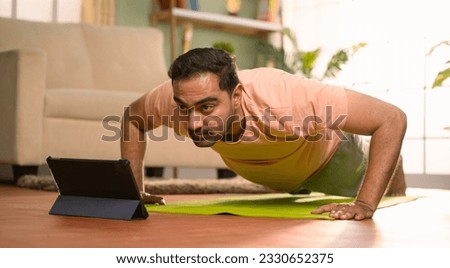 Indian man doing push ups exercise by online video classes from tablet at home - concept of Fitness instruction, Exercise Tutorial and Bodyweight Training