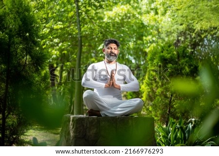 Indian man doing yoga meditation exercise in the green forest nature. fitness and healthy lifestyle. Culture and traditions of India. Hindusim or Hindu religion 