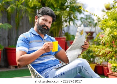 Indian man drinking tea or coffee and reading news paper - Powered by Shutterstock