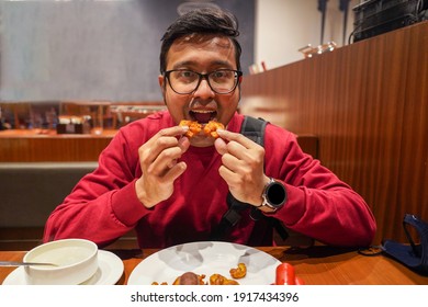 An Indian Man Eating Chicken Wings At A Cafe