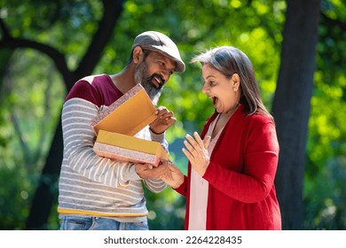 Indian man giving surprise gift to woman at park. - Powered by Shutterstock