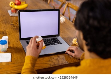 Indian man holding medication making video call using laptop, copy space on screen at home. Medical services, communication, telemedicine and healthcare, unaltered. - Powered by Shutterstock