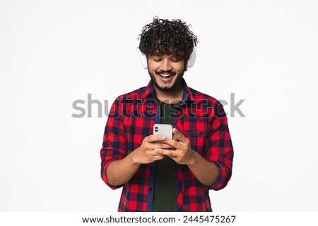 Indian man listening to the music in mobile application isolated over white background. Hindi young fan in headphones choosing track audio playlist podcast radio e-book