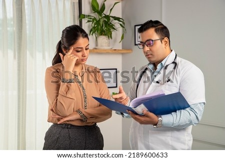 Indian man or male physician or doctor wearing stethoscope and apron holding a report file in hand and giving consultation to a tensed concerned female or Woman patient. Medical, medicine, healthcare