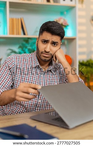 Indian man on home table looks tired closes laptop with irritation and shows burnout after routine office duties. Arabian guy on home table feels bored and exhausted from job stress in living room.