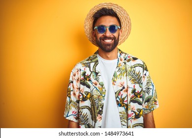 Indian Man On Vacation Wearing Floral Shirt Hat Sunglasses Over Isolated Yellow Background With A Happy And Cool Smile On Face. Lucky Person.