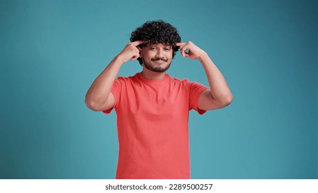 Indian man pointing his finger at his head showing high intellect and good brains and ability to think in coral t-shirt on blue studio background