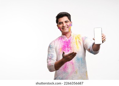 Indian man showing mobile screen on holi festival with face painted and in traditional wear.