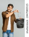 Indian man taking off throwing out glasses into bin after medical vision laser treatment therapy surgery looking smiling at camera, heal, cure. Arabian guy isolated on studio gray background. Vertical