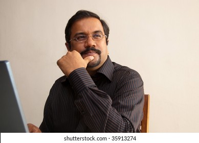 An Indian Man Thinking While Sitting In Front Of His Laptop