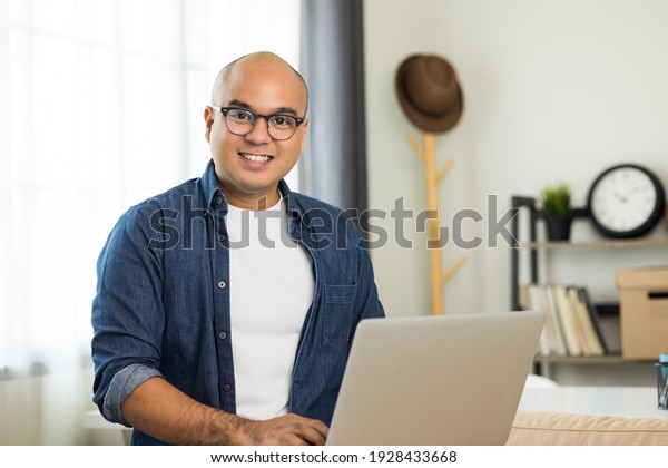 Indian man\
using laptop on sofa in living room texting on laptop sending\
message or chatting with online social\
media.