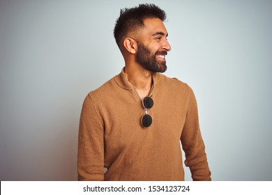 Indian Man Wearing Elegant Sweater And Sunglasses Standing Over Isolated White Background Looking Away To Side With Smile On Face, Natural Expression. Laughing Confident.