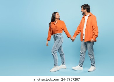 Indian man and woman in casual wear holding hands and exchanging a tender look full of connection on blue - Powered by Shutterstock