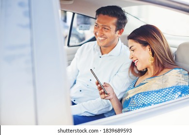 Indian Man And Woman Using Mobile Phone App To Book A Taxi, Sitting On A Passenger Seat