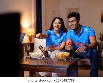 Indian man and a woman watching a live cricket match at home - World Cup match, 1-day match, Tense expression, T20 series. Couple wearing Indian jersey - face painted with Indian flag colors
