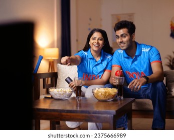 Indian man and a woman watching a live cricket match at home - World Cup match, 1-day match, Tense expression, T20 series. Couple wearing Indian jersey - face painted with Indian flag colors, watch...