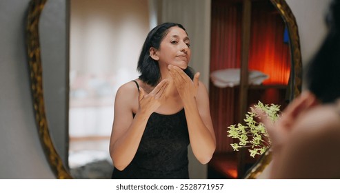 Indian mature adult gen x smiling woman after shower reflected look bathroom mirror use cosmetics beauty product apply moisturizer cream on dry face cheek do fresh skin care daily routine indoor home - Powered by Shutterstock