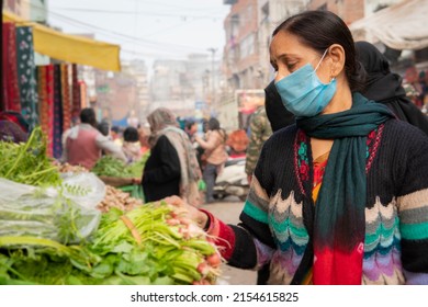 Indian Mature Woman Wearing Protective Face Mask And Buying Fresh Green Vegetables From Outdoor Market During The Third Wave Of Coronavirus, COVID-19 Pandemic Outbreak In Indian.    