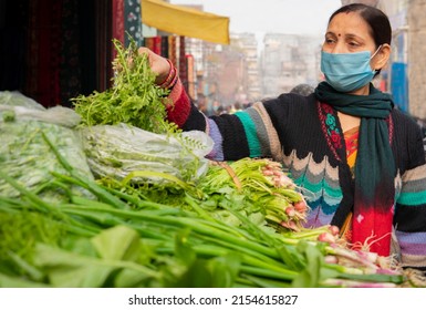 Indian Mature Woman Wearing Protective Face Mask And Buying Fresh Green Vegetables From Outdoor Market During The Third Wave Of Coronavirus, COVID-19 Pandemic Outbreak In Indian.    