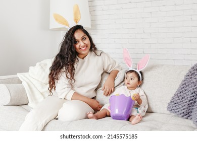 Indian mother with baby girl daughter in bunny ears playing toy eggs in basket celebrating Easter.