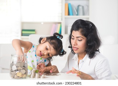 Indian Mother And Daughter Putting Coins Into Bottle, Saving Plan 