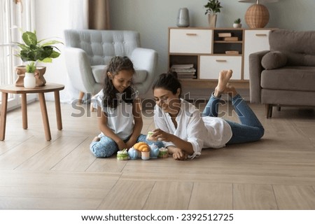 Indian mother and little daughter play together use toy set dishware and plastic sweets, spend pastime, enjoy playtime, funny creative games and communication. Leisure with children at home concept