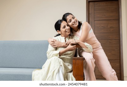 Indian Mother and Teen young daughter sitting on sofa at home looking towards the camera ,Happy Young teen hug Mother in living room - Powered by Shutterstock