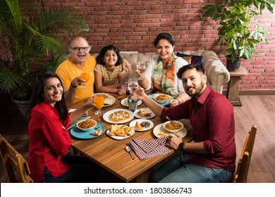 Indian multigenerational Family eating food at dining table at home or restaurant. South Asian grandfather, mother, father and two daughters having meal together - Powered by Shutterstock