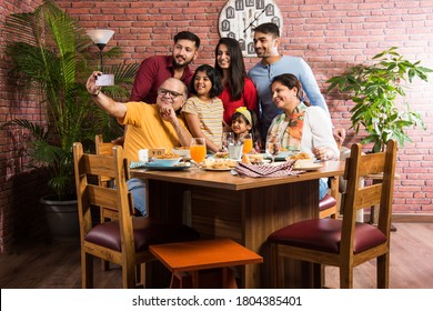 Indian multigenerational Family eating food at dining table at home or restaurant. South Asian grandfather, mother, father and two daughters having meal together - Powered by Shutterstock