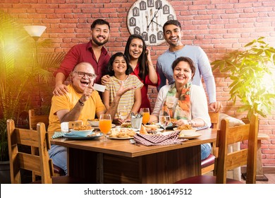 Indian Multigenerational Family Eating Food At Dining Table At Home Or Restaurant. South Asian Grandfather, Mother, Father And Two Daughters Having Meal Together