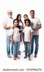 Indian Multigenerational Family In White Cloths Standing And Looking At Camera Against White Background