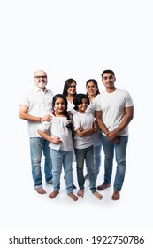 Indian Multigenerational Family In White Cloths Standing And Looking At Camera Against White Background