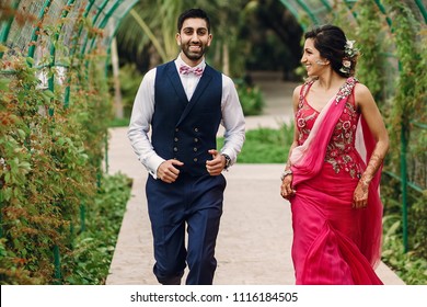 Indian Newlyweds Run Under Green Arch In The Garden