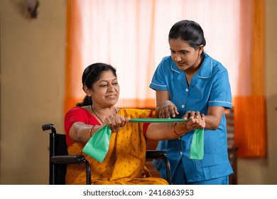 Indian nurse or therapist guiding or assisting Woman on wheelchair to stretching elastic band at home - concept of health care service, professional occupation and physiotherapist. - Powered by Shutterstock