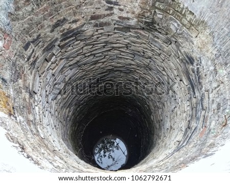 Indian old ancient medieval deep well built with rock stone boulders and reflection of sky on the water at deep bottom 