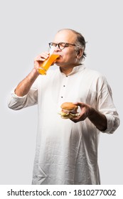 Indian Old Man Eating Burger Or Hamburger With Mango Juice Or Cold Drink