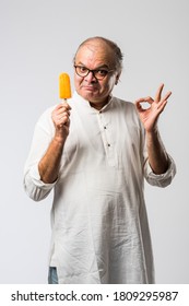 Indian Old man eating chocolate Ice cream in cone or mango candy bar